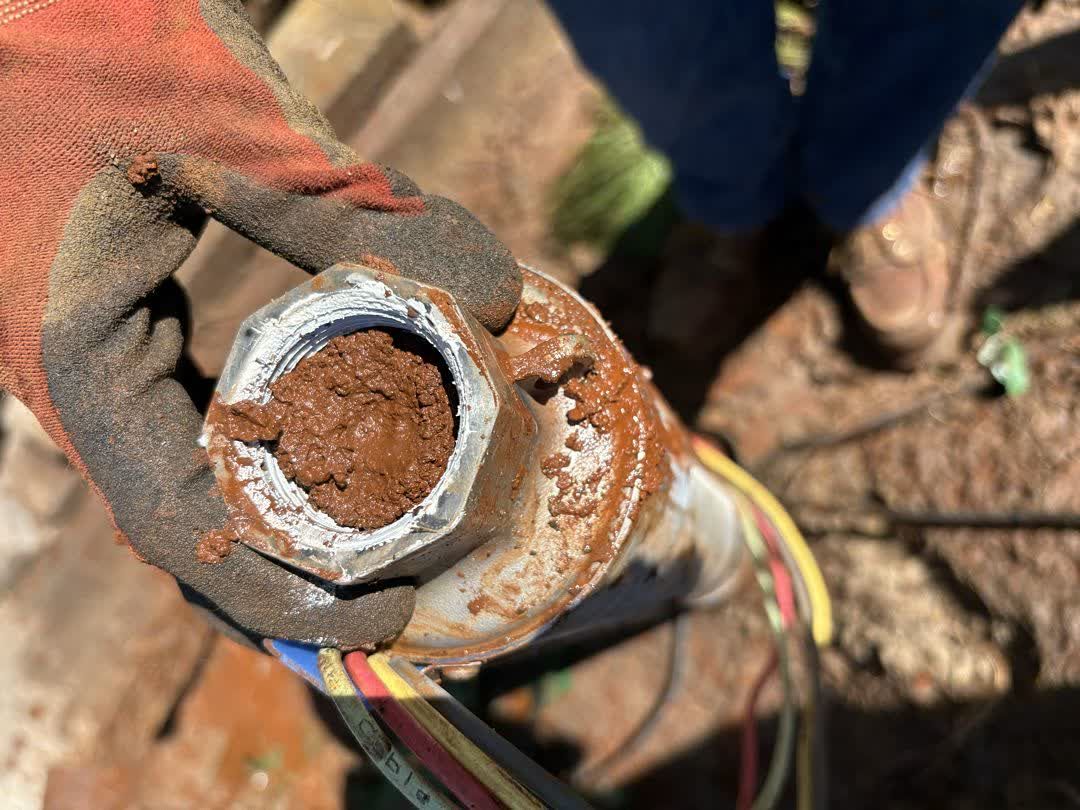 Pulled submersible pump end packed with reddish-brown sediment